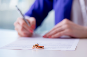 Woman signing postnuptial agreement and two wedding rings on the table.